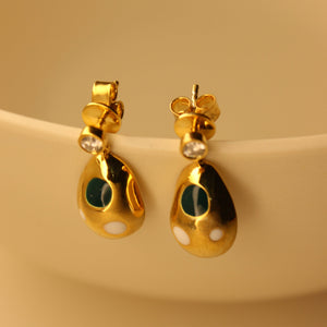Gold earrings with green and white accents on a golden surface